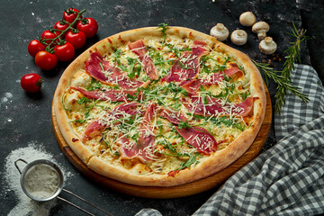 Appetizing italian pizza with cheese, prosciutto, arugula and parmesan in a composition with ingredients on a black background