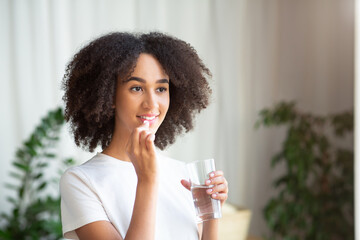 Happy smiling young african american woman taking pill or vitamin with cod liver oil omega-3