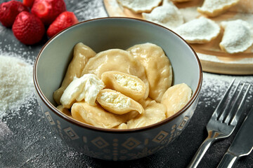 Ukrainian or Polish traditional dish - Pierogi or Varenyky (dumplings) stuffed with cheese and sour cream on a dark background. Close up, selective focus