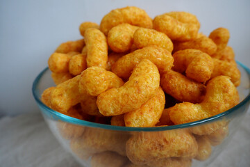 peanut flips . lots of corn sticks in peanut glaze in a glass round bowl on a gray light background with a white wall side view