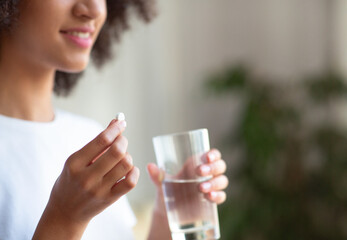 Smiling woman taking white round pill, holding water glass in hand