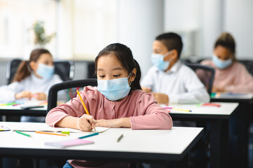 Asian girl in face mask sitting at desk in classroom