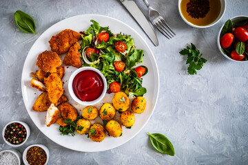 Fried breaded chicken nuggets with fried potatoes  and fresh vegetables

