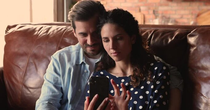 Couple read sms on smartphone celebrate great news, moment of victory concept. Wife and husband sit on couch check e-mail on device feels excited getting fantastic offer discount low price concept