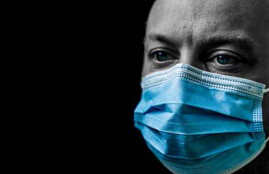 Sick Man With Bright Blue Eyes Wearing A Facemask, Portrait Isolated On Black With Shallow Depth Of Field.