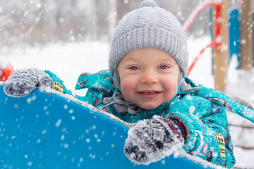 A little cute boy in a warm jumpsuit is playing on the playground outside in winter. Happy childhood. Game