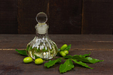 Neem oil in bottle and neem leaf with fruit on wooden background.