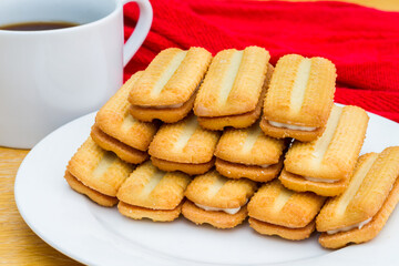 Fototapeta na wymiar Several viennese finger biscuits with a butter cream filling on a white plate with cup of coffee the background.