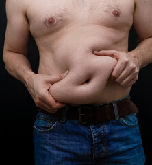 Man with extra weight on his belly grabs his skin. Isolated on black background.