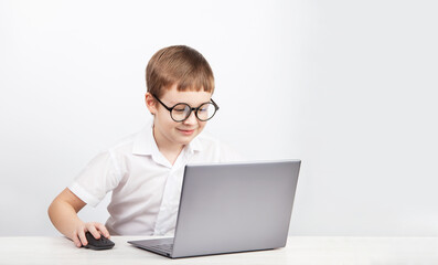 a boy with glasses, an elementary school student, sits at a table with a laptop on a white background