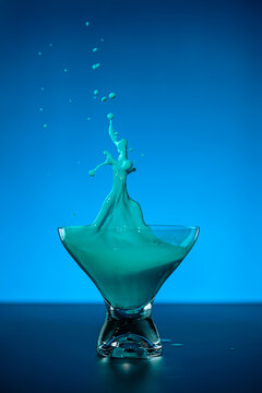 colorful alcoholic healthy drink falls on the table with the glass and splashes in the air on blue background