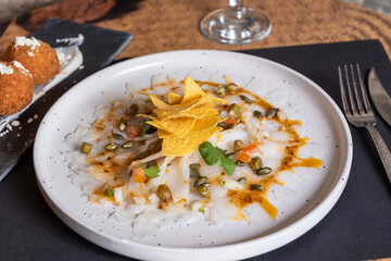 White plate with Cod Carpaccio with chili vinaigrette, pumpkin seeds and chips.