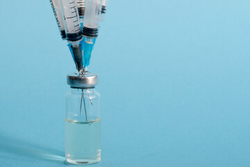 Close-up of a bottle of vaccine, and five medical needles with injections stuck in the bottle cap on a blue isolated background. The concept of a shortage of medicines for coronavirus