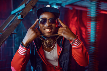 Smiling rapper with gold chain posing in studio - obrazy, fototapety, plakaty