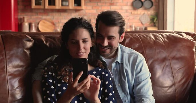 Young couple resting sit on couch using smartphone having fun use new cool mobile application, taking selfie, making photo portraits smiling spend free weekend time at home. Modern tech usage concept