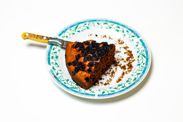 A piece of chocolate cake on a white plate with blue ornate patterns. Brownie. Cake. White background. Knife. Crumbs. Disorderly. Blueberry pie. Cake. Selective focus