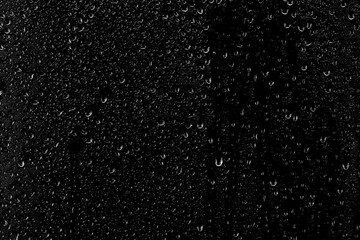 Obraz premium Drops of water flow down the surface of the clear glass on a black background. Texture for creativity.