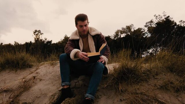 Ragazzo legge un libro seduto in spiaggi in inverno