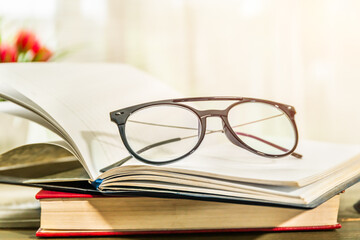 Reading glasses put on open book beside the window