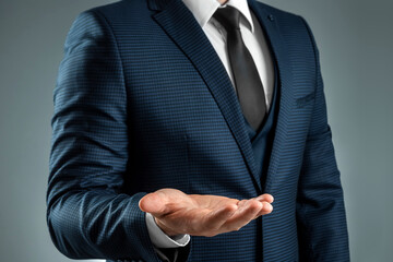 Male hand in a suit shows a palm up gesture on a gray background. Concept of request, bankruptcy,...
