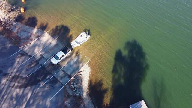 Pickup truck pulling boat and trailer out of the water at the shore of a lake.