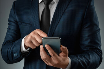 A businessman in a business suit holds a smartphone in his hands. Uses the Internet to work and communicate with partners. Online business concept, remote work, freelance. Close-up.