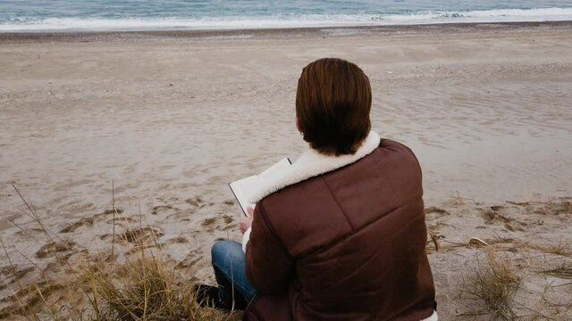 Ragazzo legge un libro seduto in spiaggi in inverno