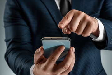 A businessman in a business suit holds a smartphone in his hands. Uses the Internet to work and communicate with partners. Online business concept, remote work, freelance. Close-up.