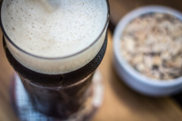 Black porter stout bock beer with foam in pint glass with peanuts on a wooden table