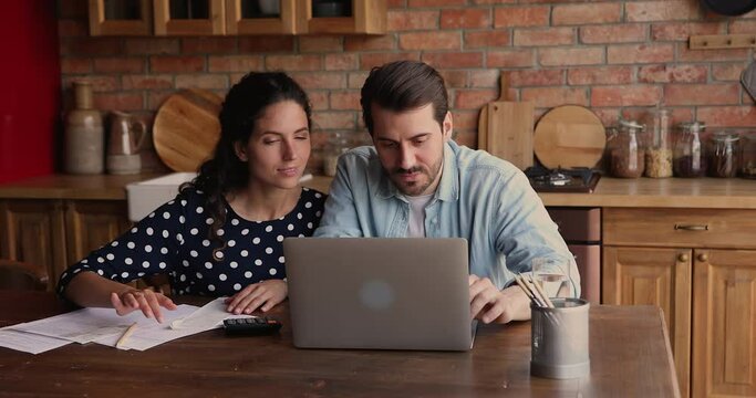 Married couple sit in kitchen at home check receipts, paying monthly domestic utility bills using e-bank application on laptop, provide monthly remittance. Family budget plan and management concept