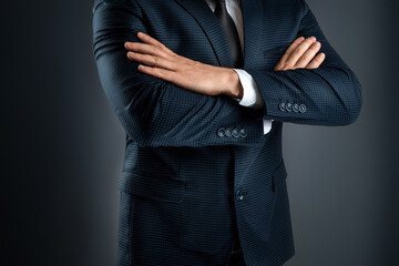 A man in a business suit stands with his arms crossed on a gray background. Concept businessman, business communication. Close-up.