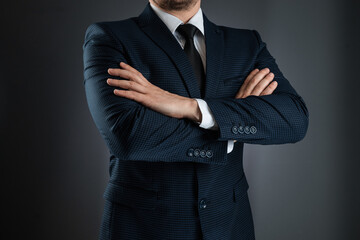 A man in a business suit stands with his arms crossed on a gray background. Concept businessman, business communication. Close-up.