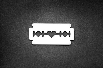 Mirror surface razor blade with a heart-shaped opening in the middle on a black backdrop