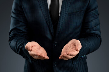 Male hand in a suit shows a palm up gesture on a gray background. Concept of request, bankruptcy, close-up.