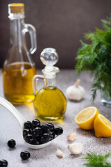 olive oil in glass bottles next to olives, dill, lemon and garlic on the table
