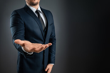 Male hand in a suit shows a palm up gesture on a gray background. Concept of request, bankruptcy,...