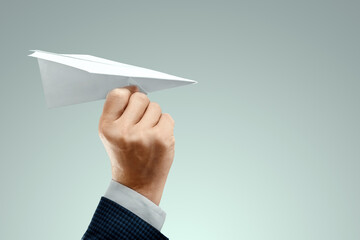 A man's hand in a business suit holds a paper airplane. Startup concept, light business, getting started. Copy space.