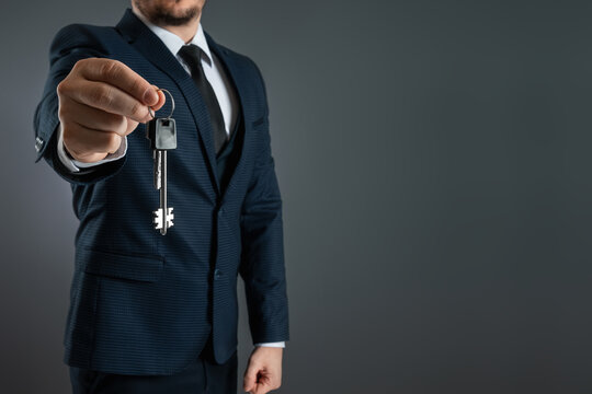 A Man In A Business Suit Holds Out The Keys In His Hand. The Concept Of A Realtor, Mortgage, Your House, Home Loan. Copy Space.