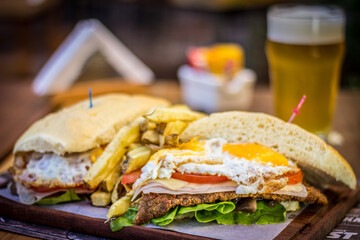Milanesa argentinian steak sandwich with salad tomatoes cheese egg, chips and beer