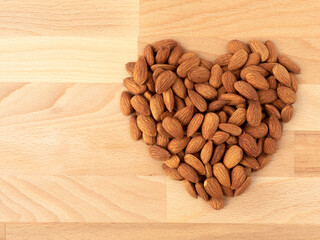 Heap of organic almonds in heart shape top view on wooden background with copy space for concept of...