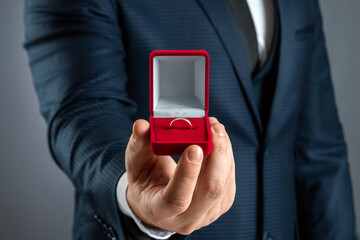 Will you marry me, A man in a business suit holds out in his hand a red box with a wedding ring. Concept of marriage proposal, wedding, marriage. Close-up.