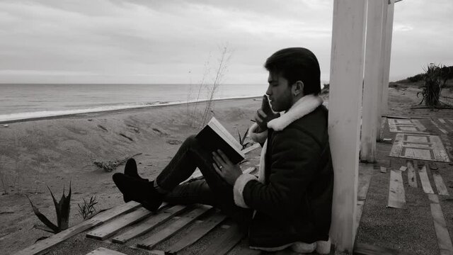 Ragazzo legge un libro e fuma una sigaretta seduto in riva al mare in spiaggia