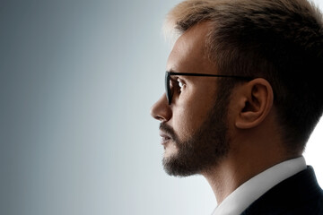 Close-up portrait of a man with glasses sideways in profile looking at the light from the dark. Neutral facial expression, copy space.