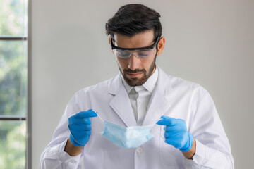 Close up male doctor, researcher, scientist wearing eye protection glasses, white suit, glove and...