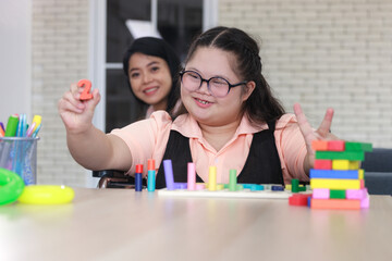 young girl with autism is practicing fun playing with toys at home with his mother. Autistic young students are learning with teachers happily.