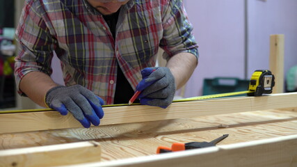 A man measures a piece of wood with a tape measure. A man makes home repairs. Builder, repairman with karashdash draws on the board