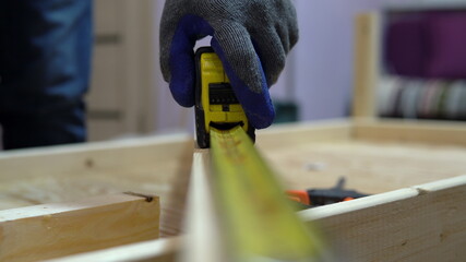 A man measures a piece of wood with a tape measure. A man makes home repairs.