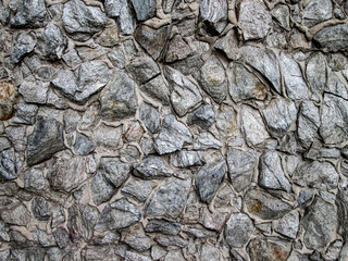 Gray cobblestones in the concrete wall. Decorative surface with stones.