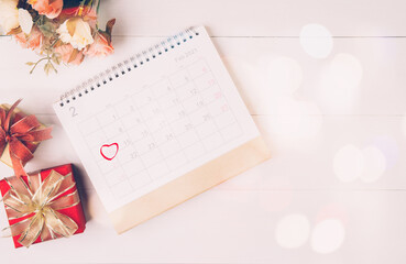 Calendar and flower with memo 14 February Valentine day on desk with blur bokeh background, reminder for surprise of love, romance and sweet, celebration and decoration, top view, holiday concept.