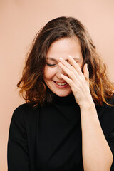 Laughing middle aged woman with her eyes closed, hand covering face. She has subtle cat eye makeup, she wears black shirt